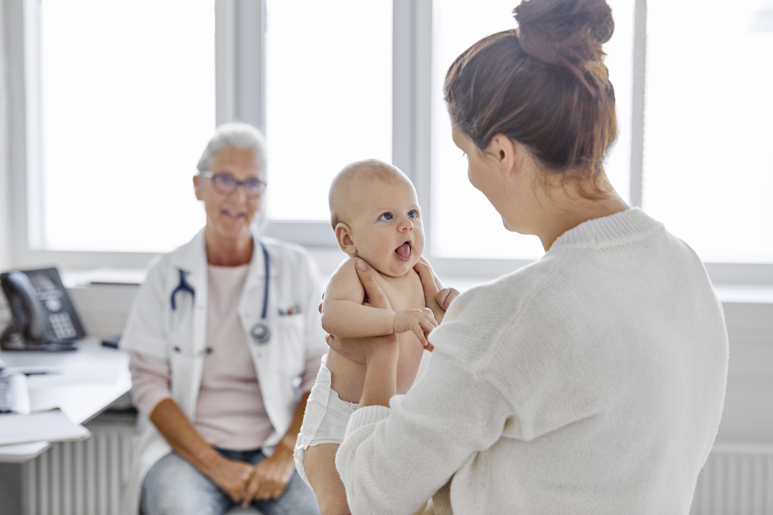 Äiti pitelee hyväntuulista vauvaa sylissään lääkärin vastaanotolla