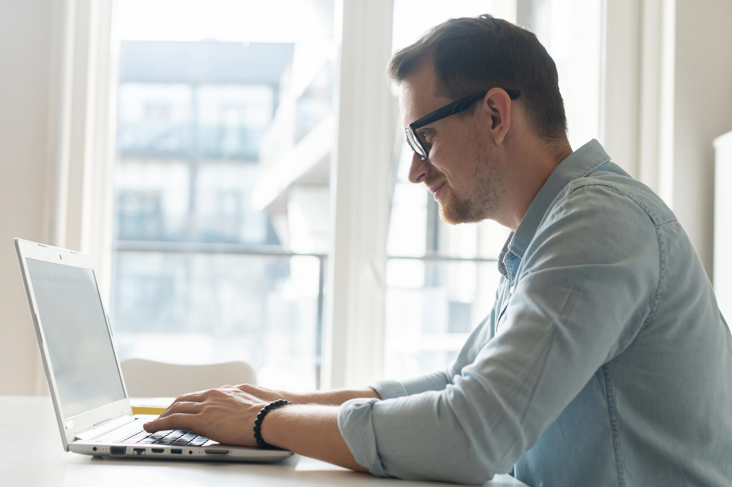 Mieslääkäri istuu tietokoneen ääressä ja hymyilee